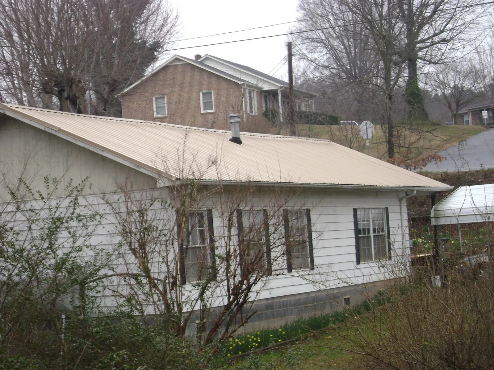 Tan metal roof on a white sided house set into a hillside — Commercial Roofing by Roofing Brothers in Kaneohe